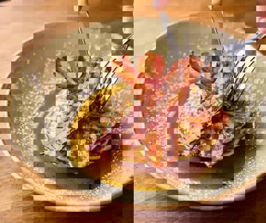 A knife and fork cutting into a stack on pancakes topped with streaky bacon and maple syrup